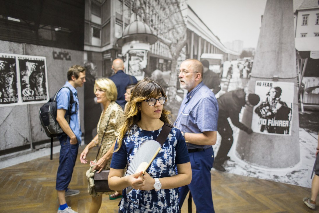 Visitors viewing black and white historical photographs and posters displayed on walls in a gallery exhibition space.