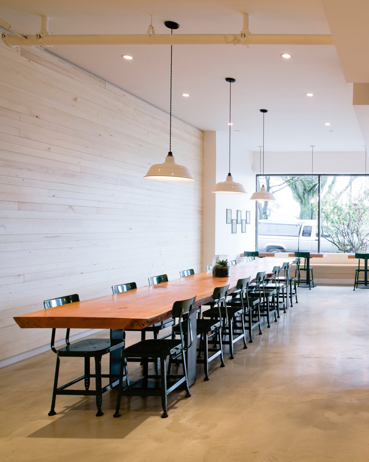 Matchstick café interior with long wooden table, black chairs, white shiplap wall, and pendant lights in Vancouver.