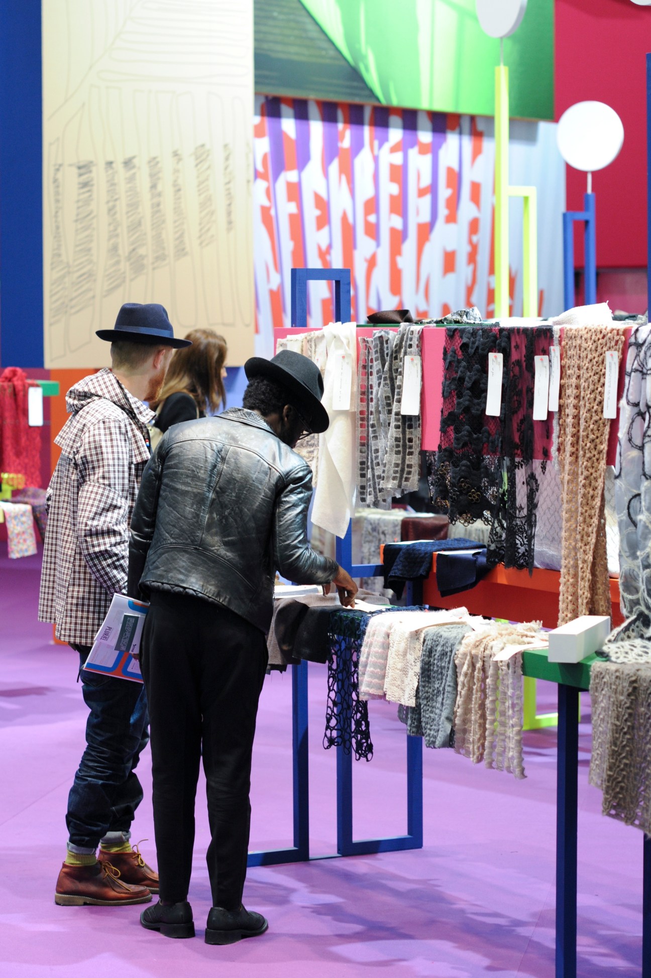 Visitors examine fabric swatches displayed on racks at a colorful textile fair booth.