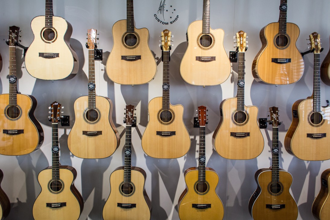 Multiple Maton acoustic guitars displayed on a white wall, showing various wood finishes and styles.