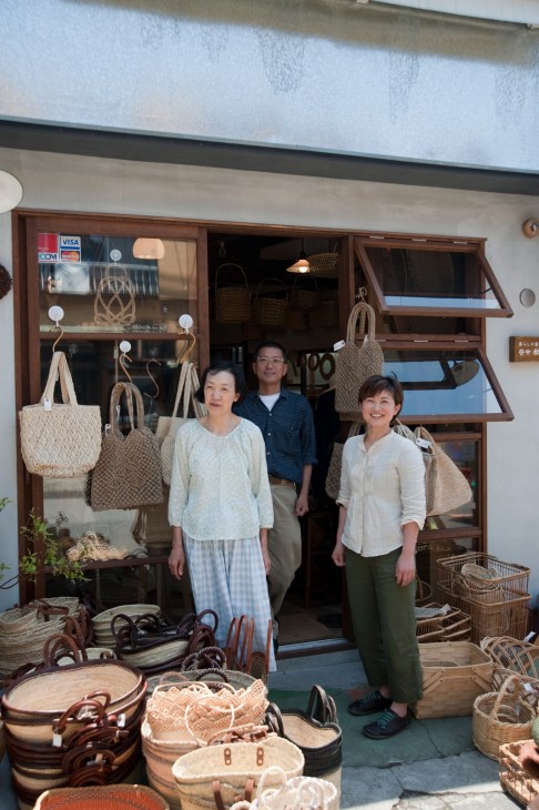 Three people stand outside Matsunoya storefront displaying handmade baskets and bags.
