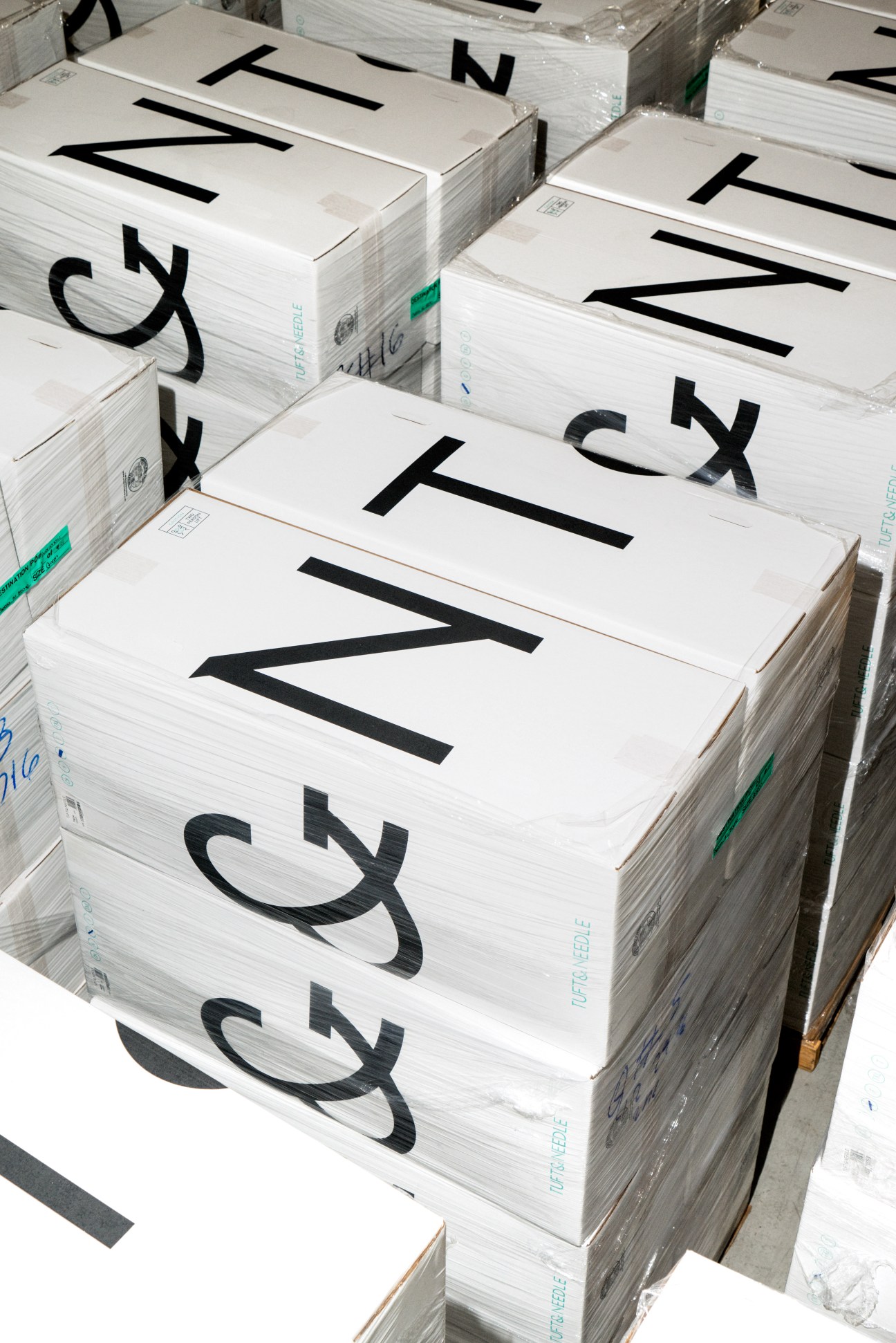 Stacked compressed mattresses in white boxes with black branding at Tuft & Needle's Phoenix warehouse.