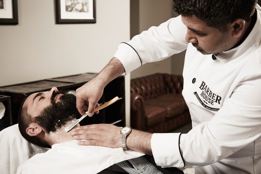 A barber at Barber House in Munich applies shaving cream to a customer's face with a brush.