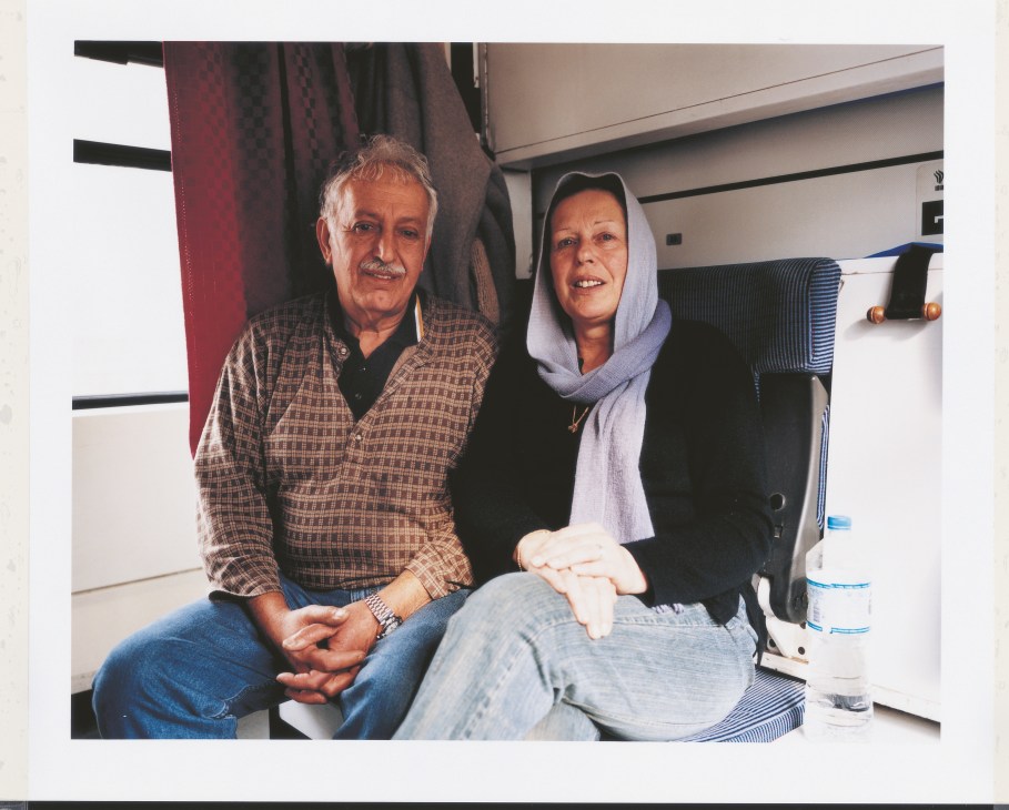 Bemrouz and Sue Moorian sit together in a train cabin, with luggage visible in the background.