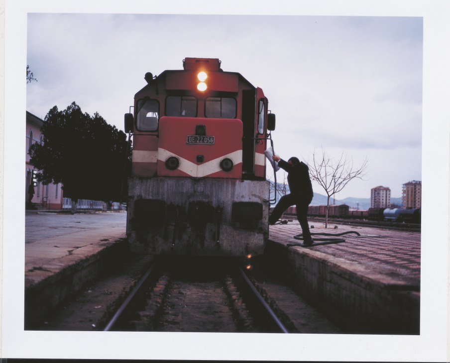 Train driver stretching beside red and white locomotive at Kayseri station during TransAsya Express journey.