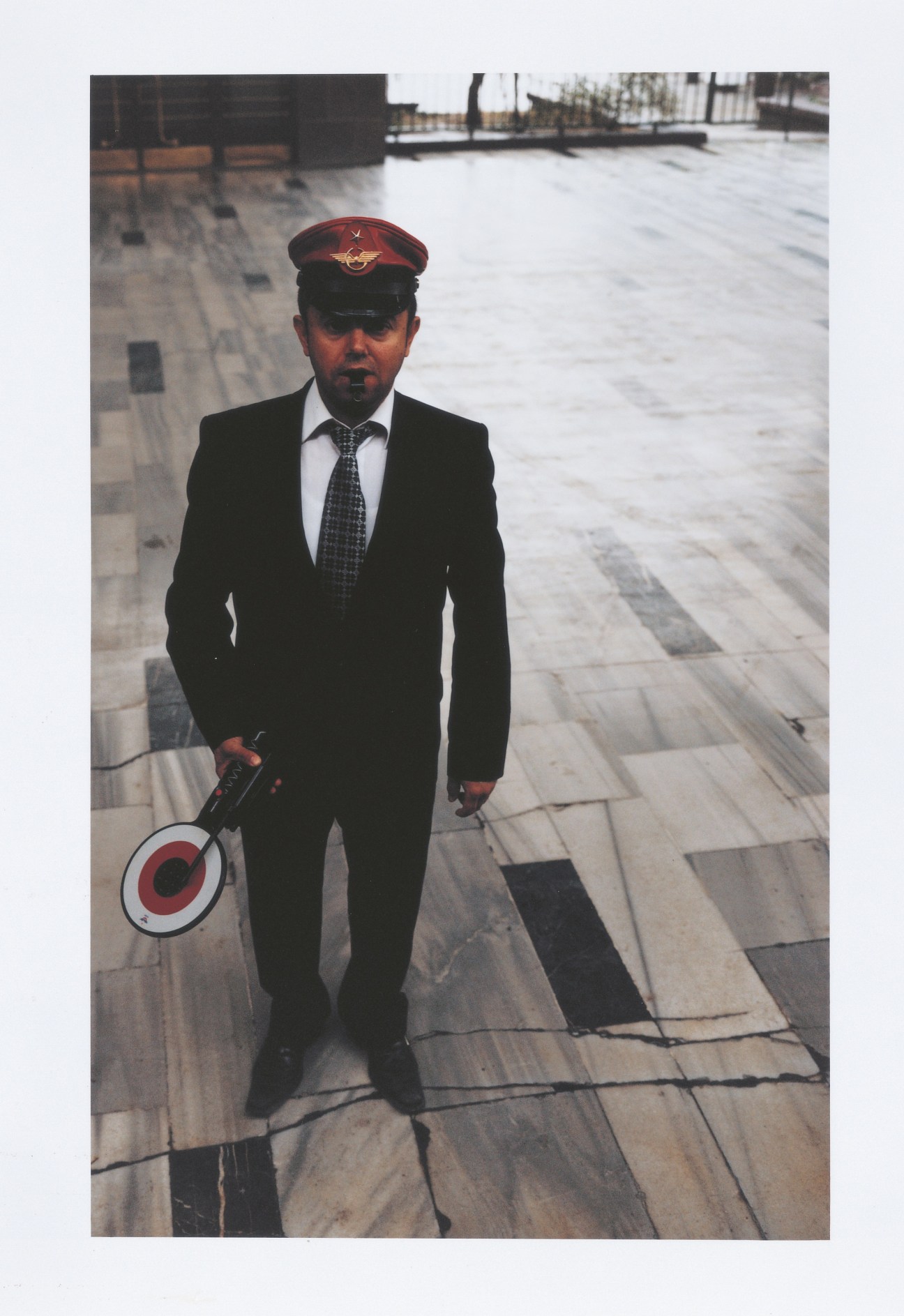 A train conductor in uniform standing on a platform at Ankara station holding a red and white signal disc.