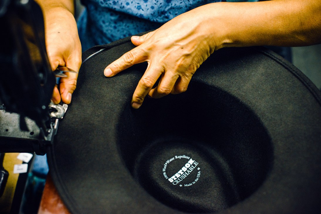 Factory worker's hands applying finishing touches to a black Stetson hat bearing 'Made in the USA' label