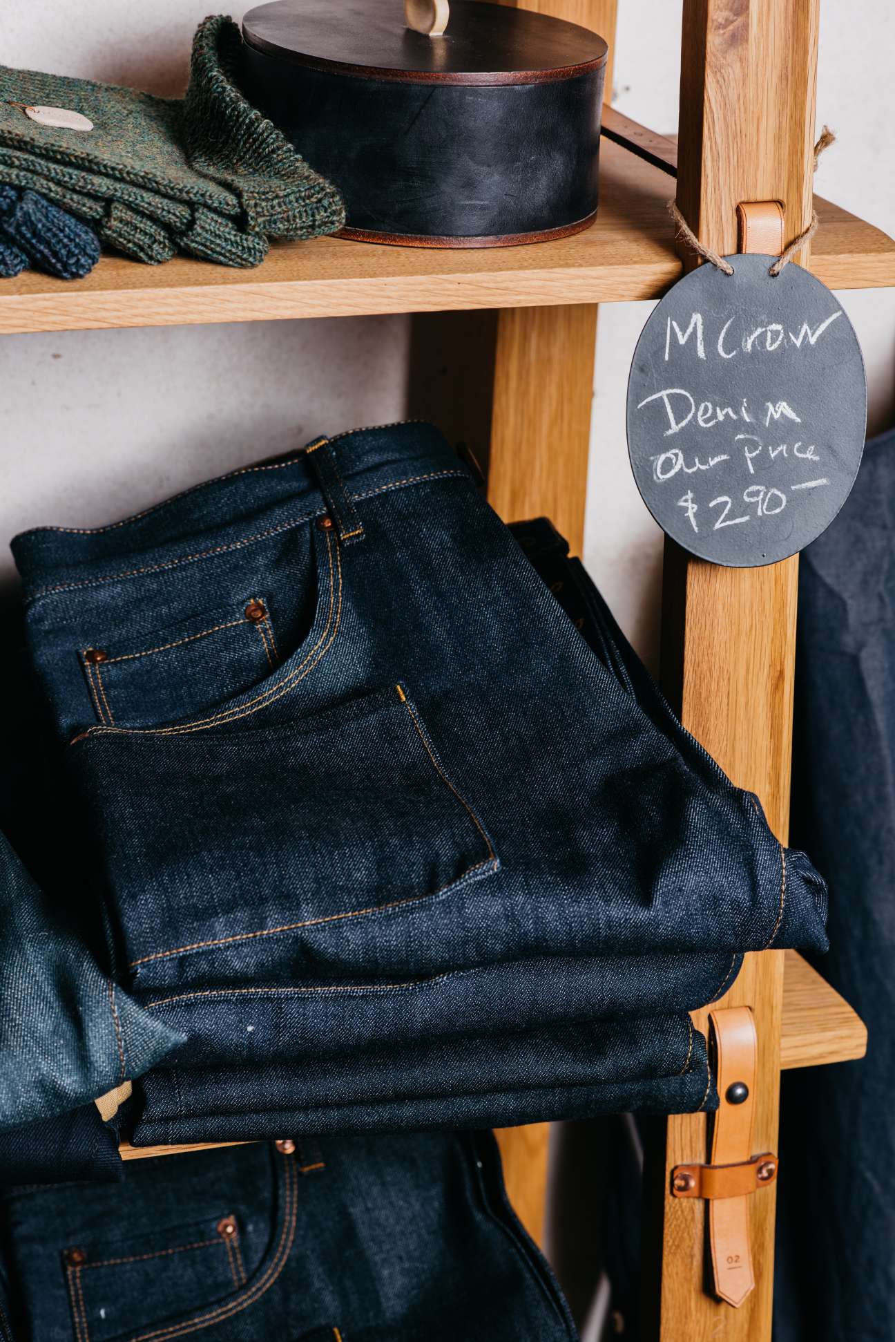 M Crow denim displayed on wooden shelf with price tag and knitted items above.
