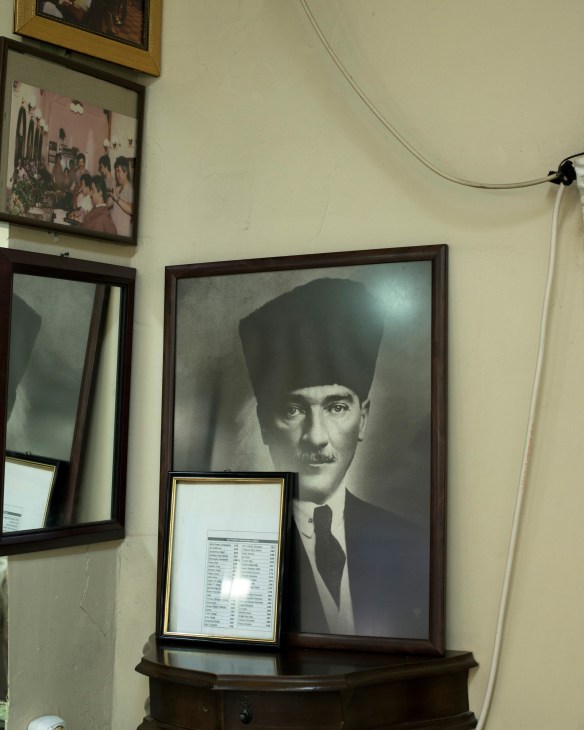 Portrait of Mustafa Kemal Ataturk in a tall black fez and suit displayed on a barber shop wall.