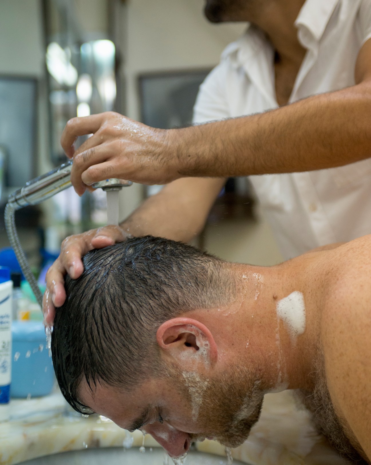 Barber apprentice washes customer's hair at sink in Istanbul barbershop.