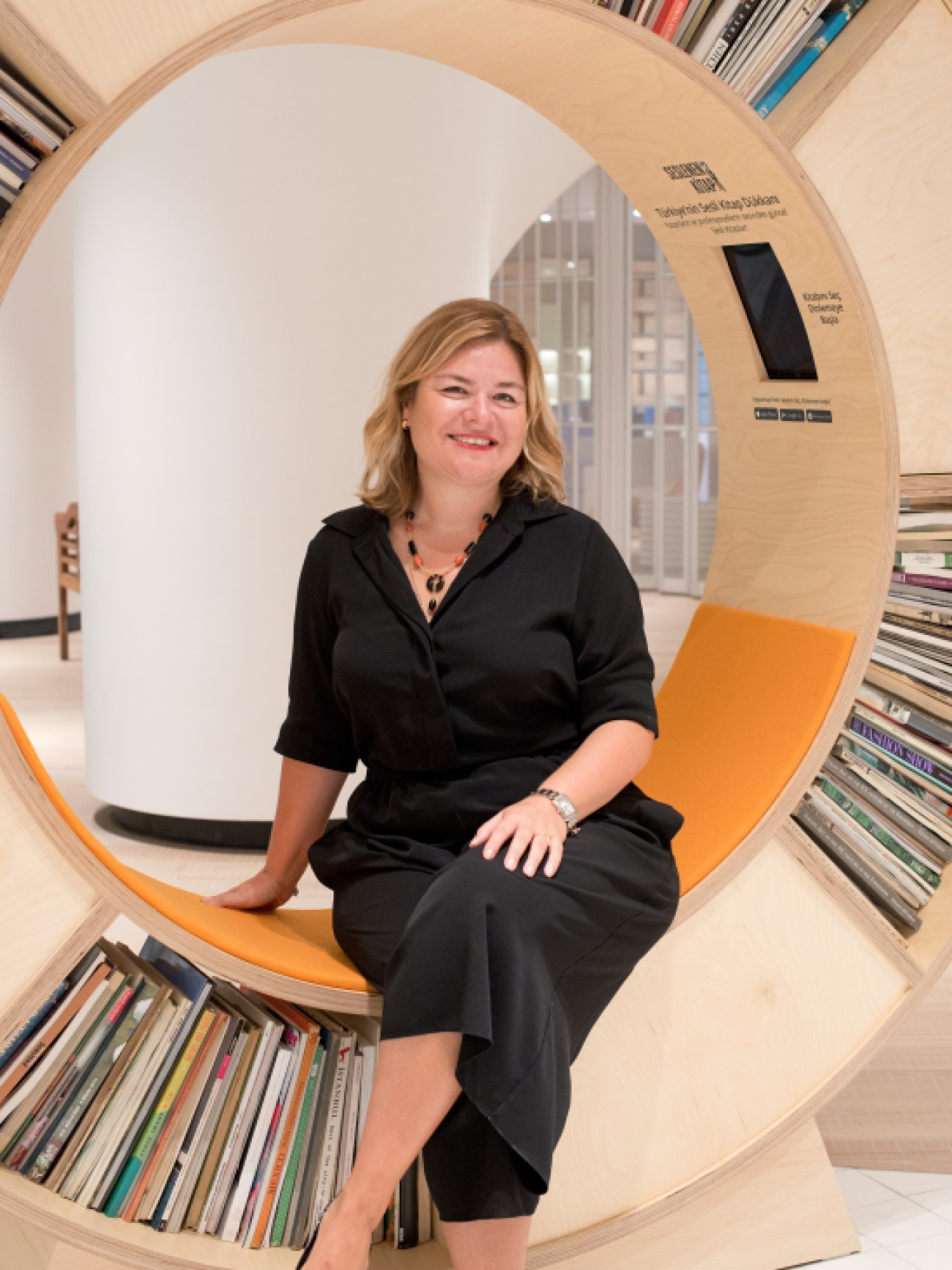 Elif Capci, CEO of Beymen, sits in a circular wooden chair with orange accents surrounded by bookshelves.