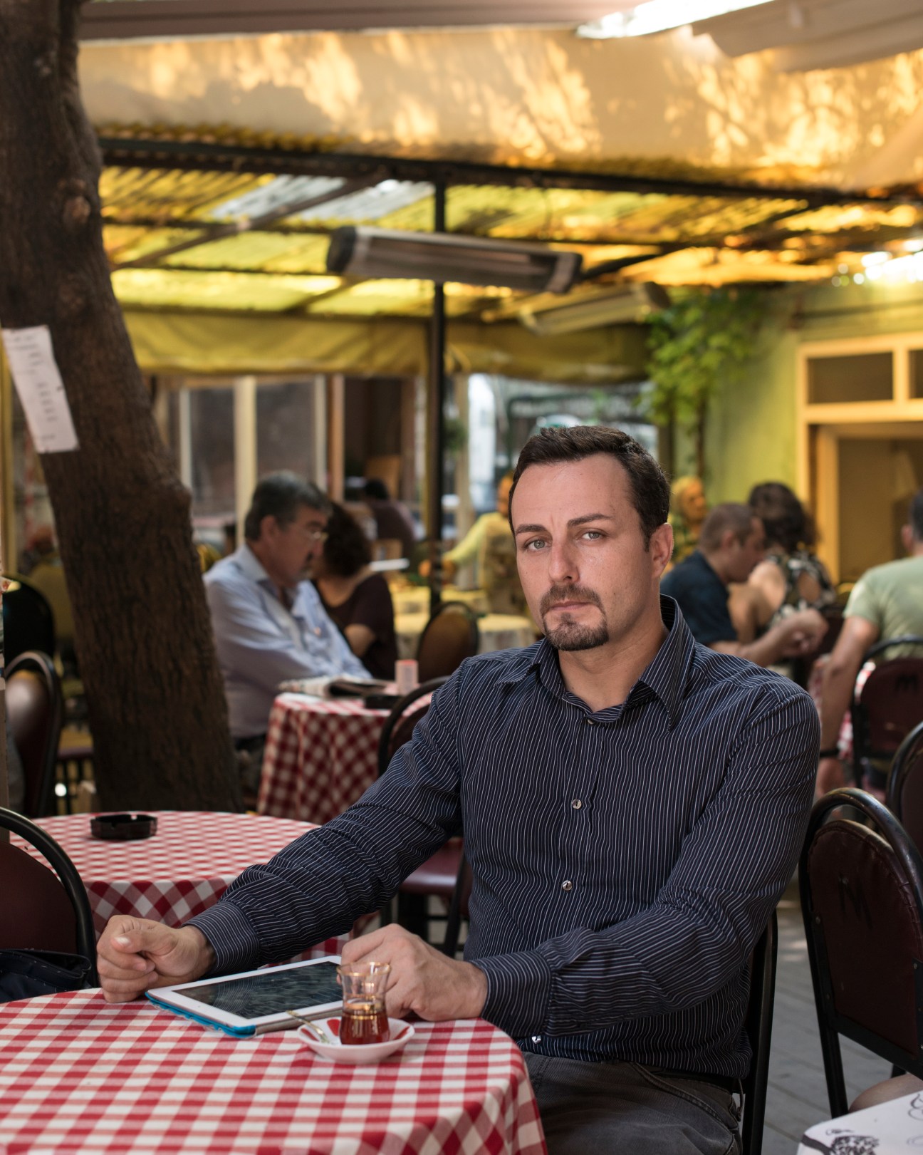 Tarek Chazli, an Italian diplomat of Syrian origin, sits at a café table holding a tablet.