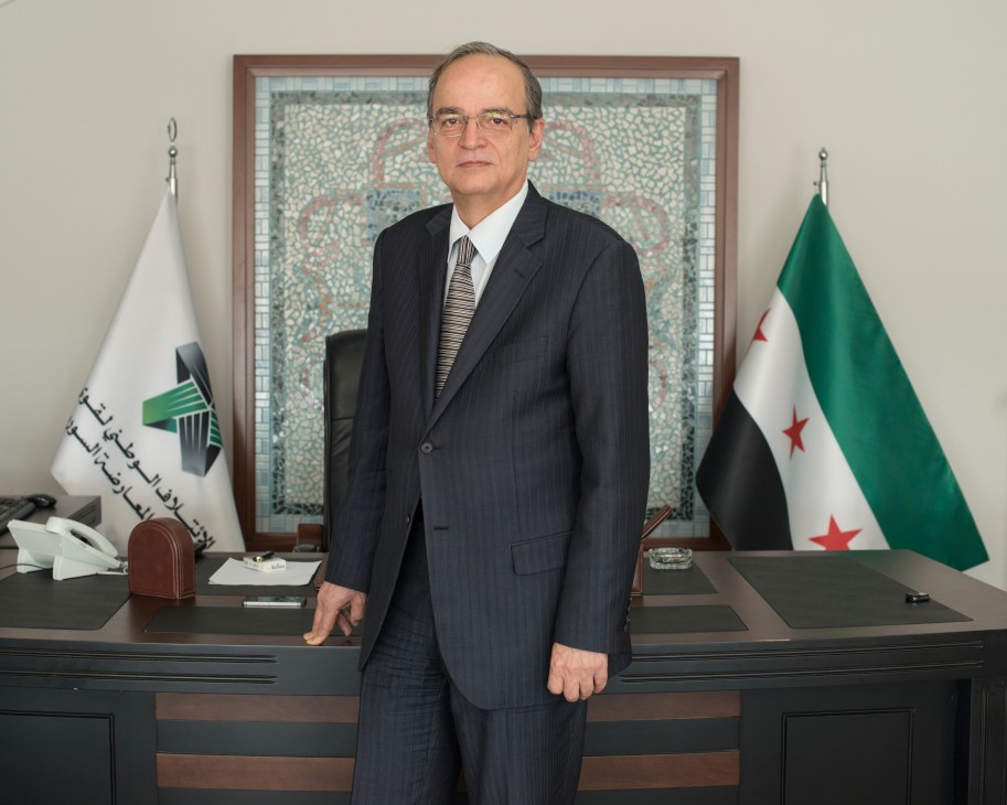 Etilaf president Hadi Al Bahra stands in formal office setting with Syrian opposition flags.