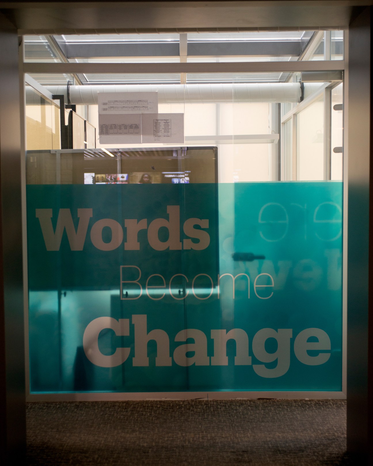 Turquoise glass panel with text reading 'Words Become Change' displayed in a modern studio setting.