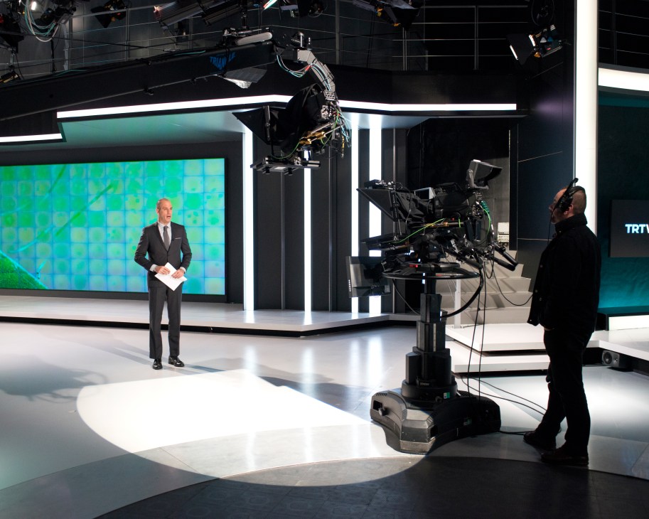 Alican Ayanlar stands on the TRT World news studio set during broadcast production.