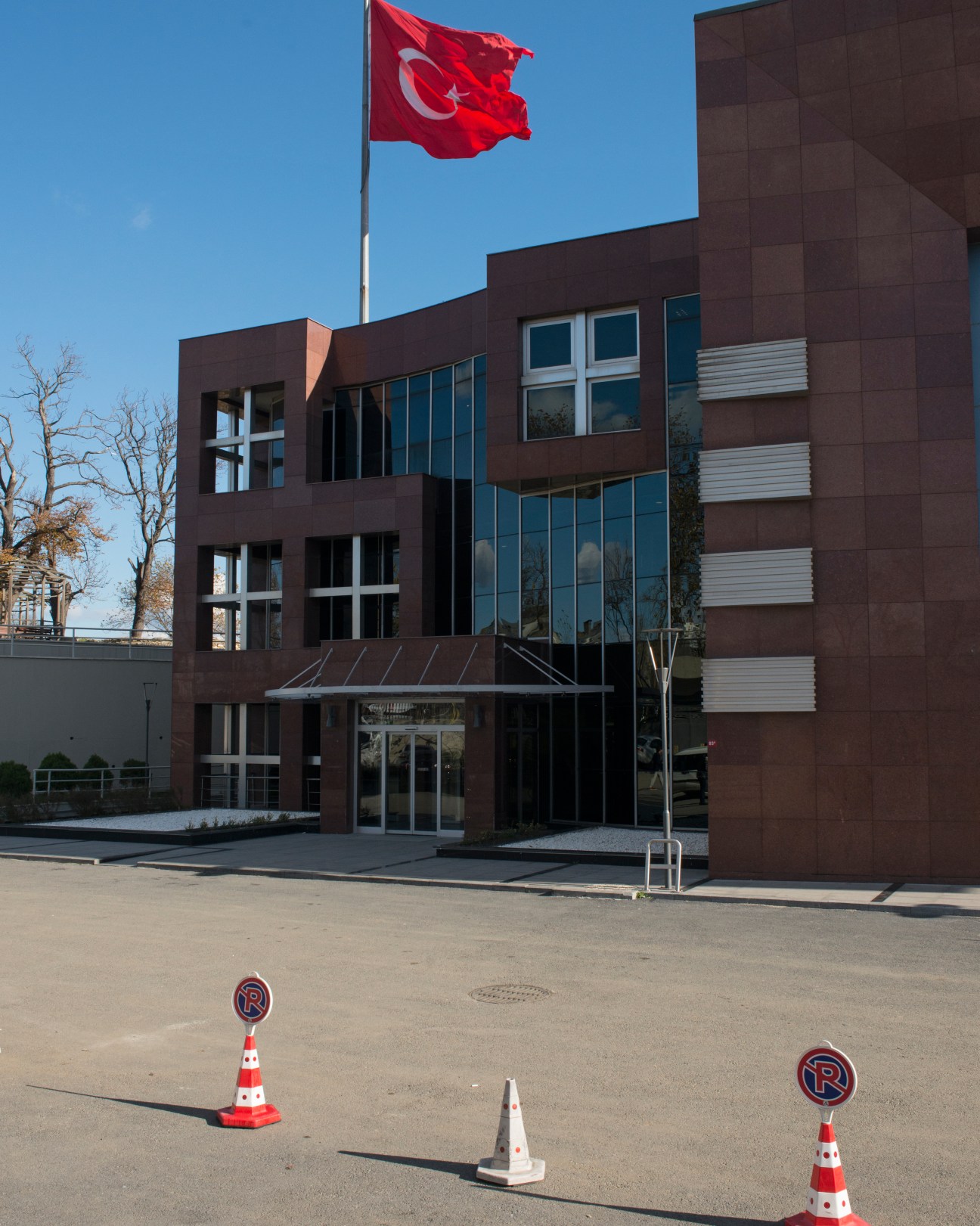 Turkish flag flying above a modern brown brick building with blue-tinted windows.