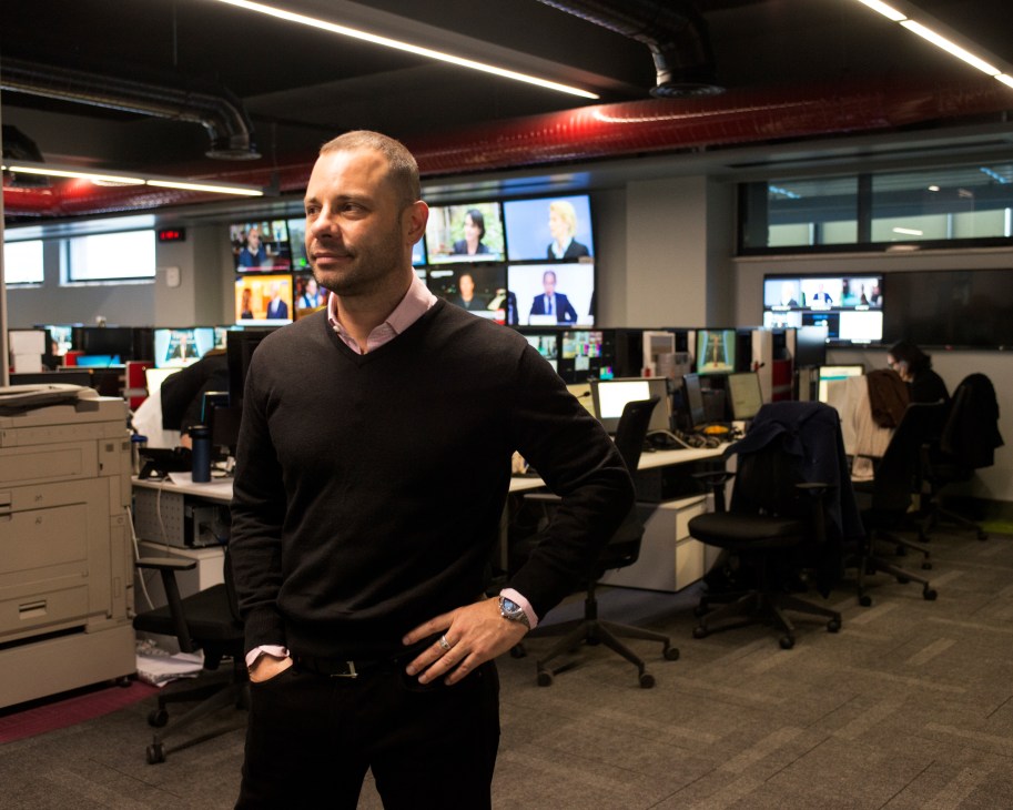 J Carlos Van Meek, director of news at TRT World, stands in the newsroom with multiple screens visible behind him.