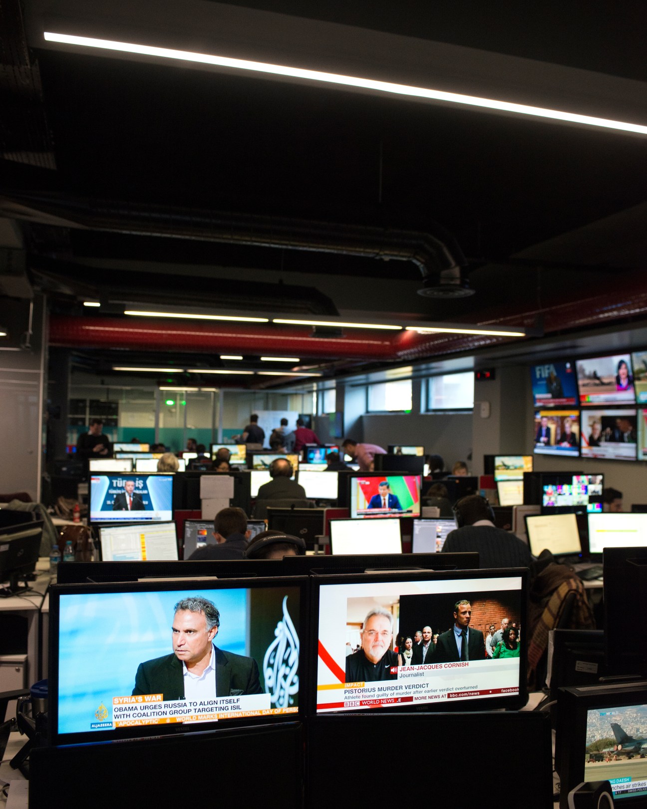TRT World newsroom with staff at desks monitoring multiple screens displaying news broadcasts and content.