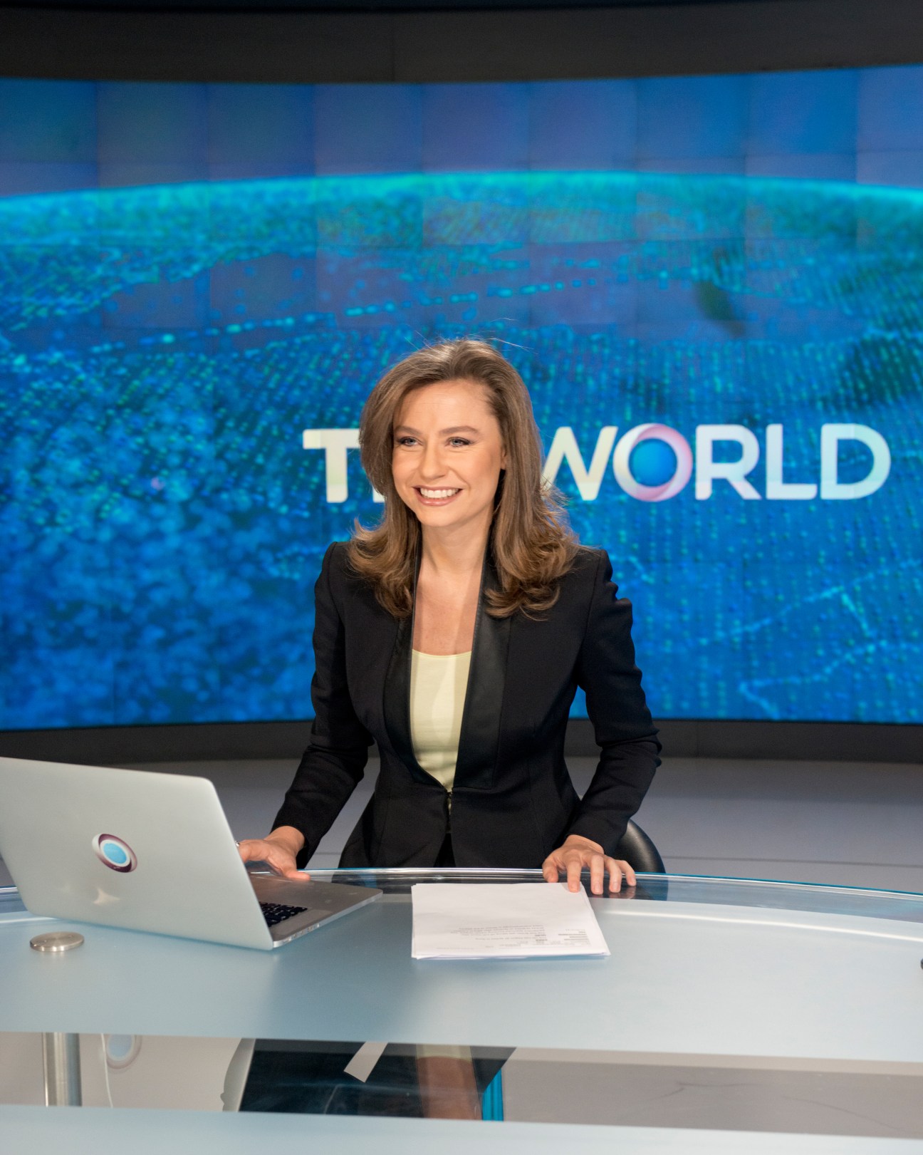 Andrea Sanke at TRT World newsdesk with turquoise branded backdrop behind her.