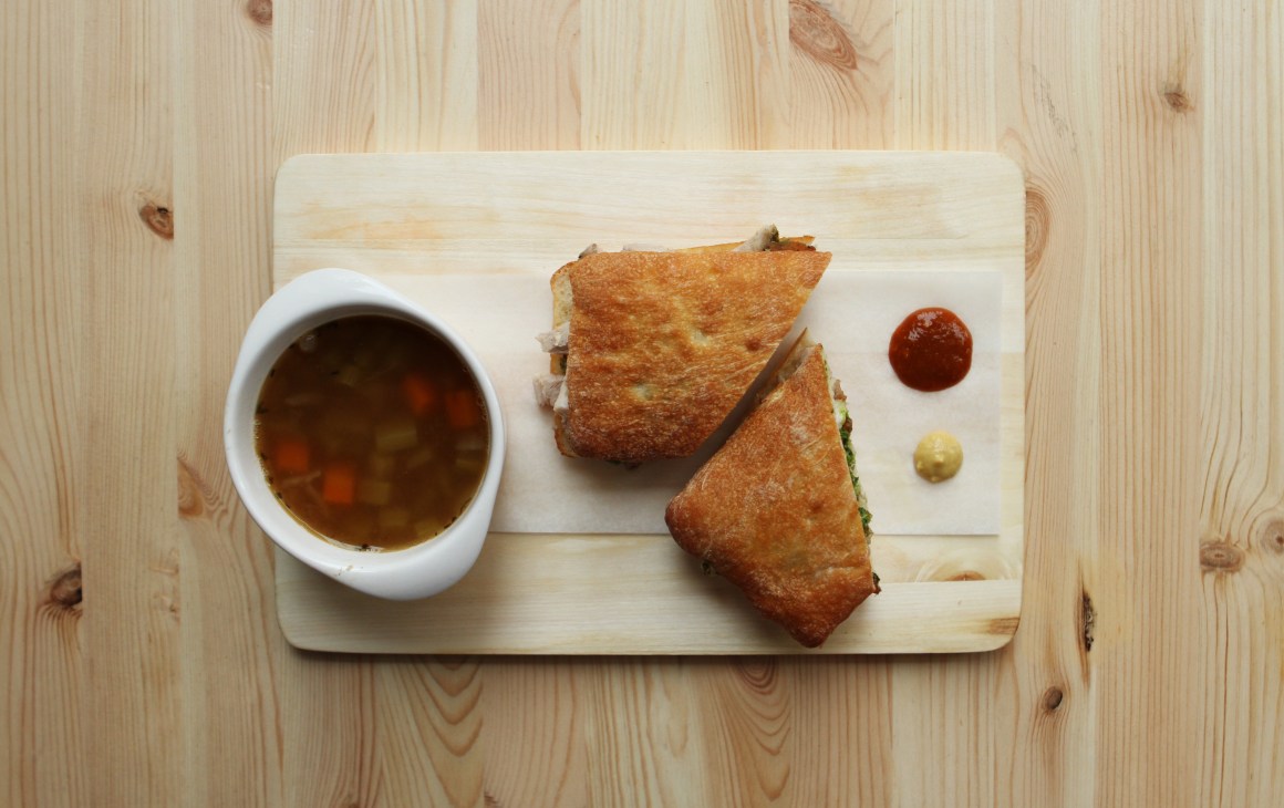 Two golden fried meat sandwiches on a wooden board with dipping sauce and condiments.
