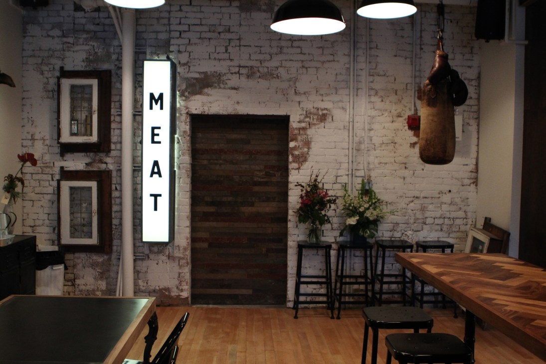Interior of Meat & Bread restaurant with exposed brick wall, wooden tables, and 'MEAT' sign.