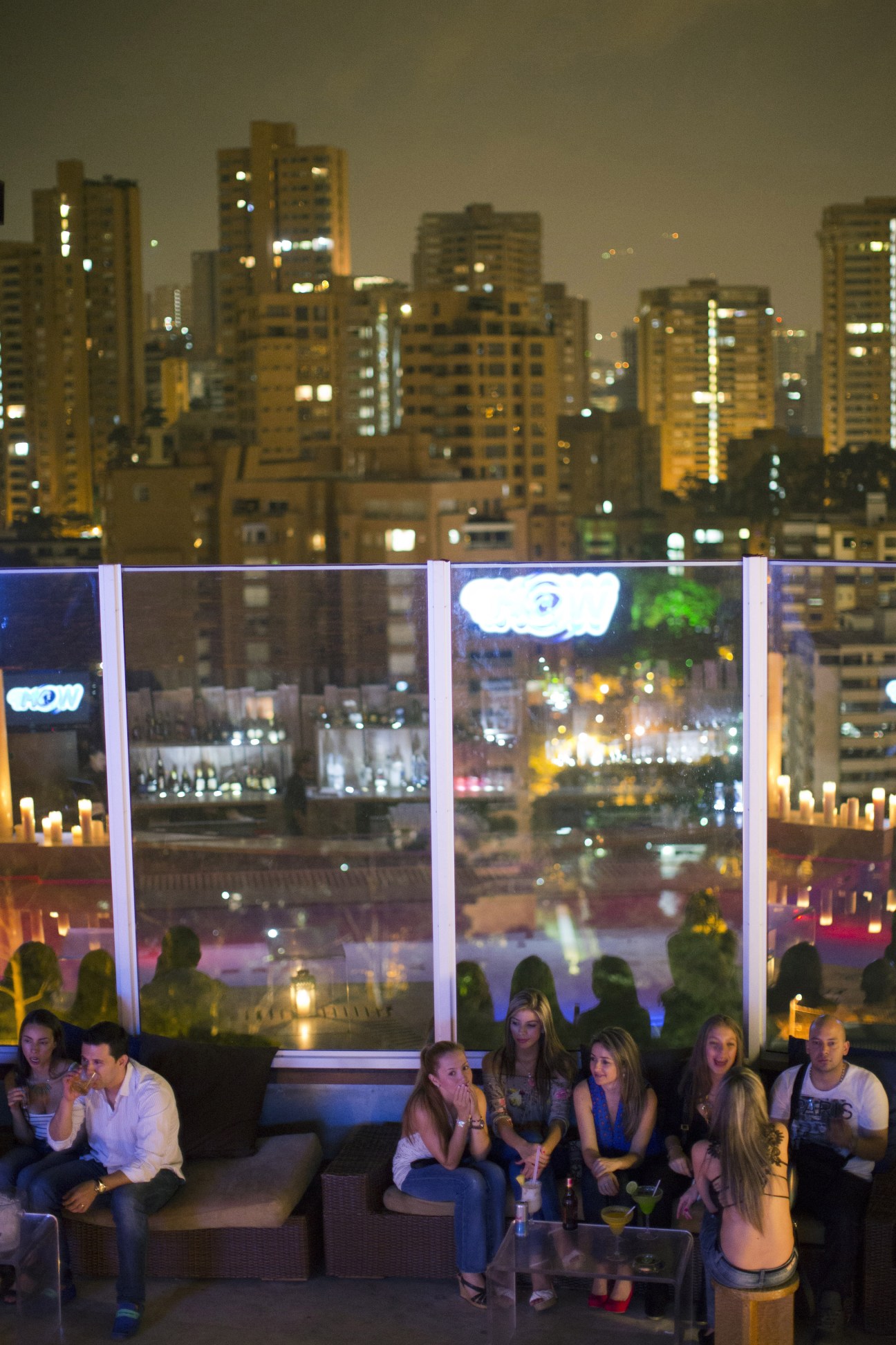 People seated on couches in Envy nightclub overlooking illuminated Medellín cityscape at night.