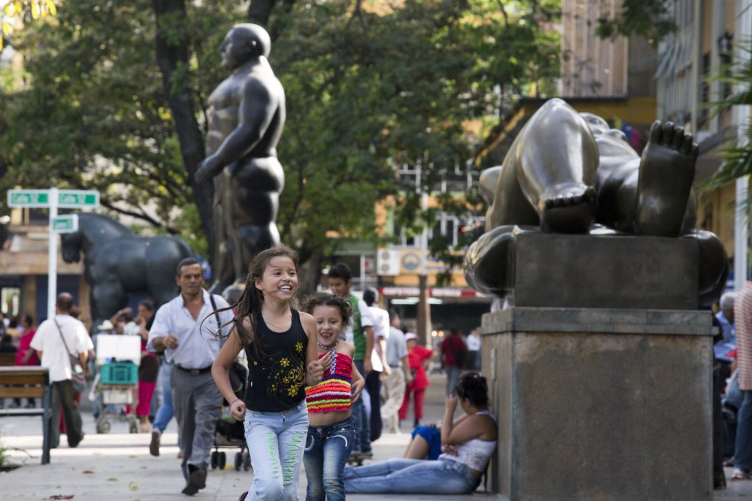Children playing near large black sculptural figures in Plaza Botero, Medellín's public square.