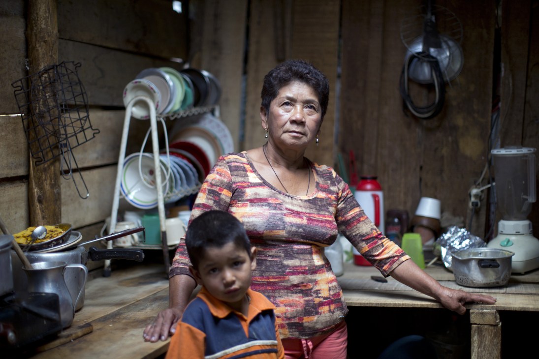 Monica Benitez, a displaced mother, stands in her modest kitchen with a child in a slum neighborhood.