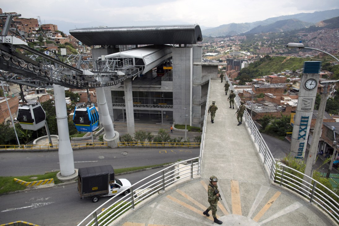 Modern cable car station with soldiers standing on an elevated platform overlooking a hillside slum in Medellín, Colombia.
