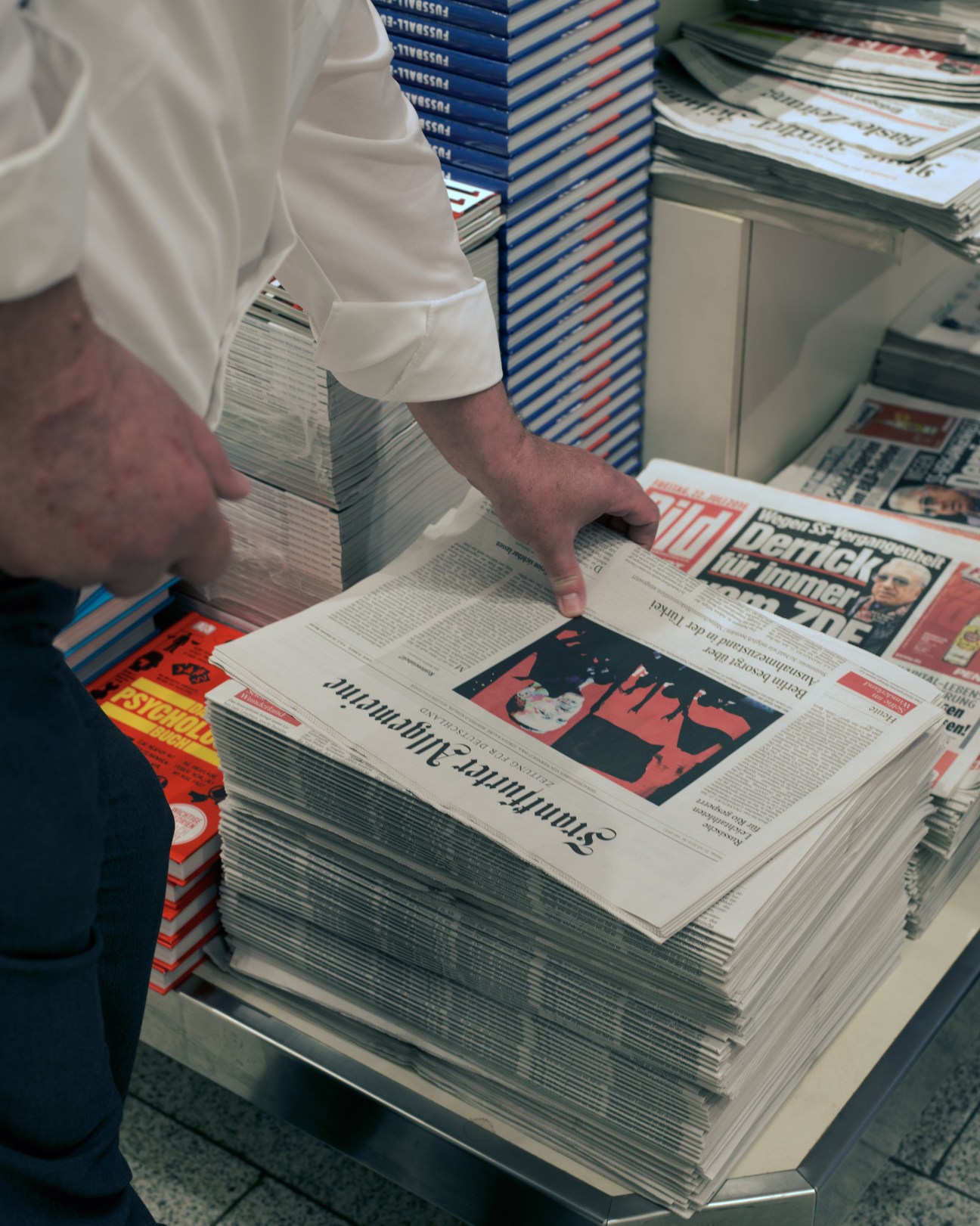A person in a white shirt browses copies of Frankfurter Allgemeine Zeitung newspaper on display.