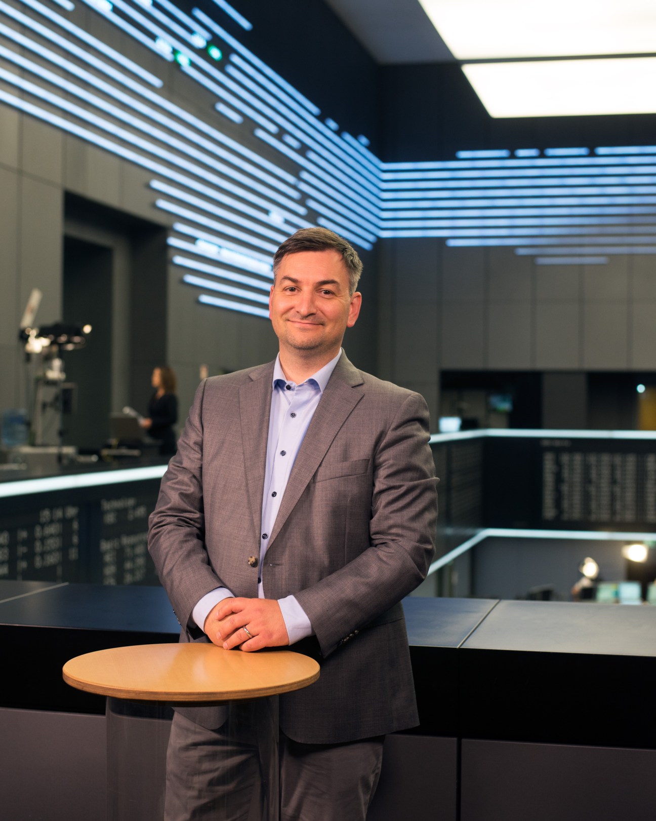 Markus Gürne, presenter of 'Börse vor Acht', stands at a desk in a modern television studio with blue lighting.