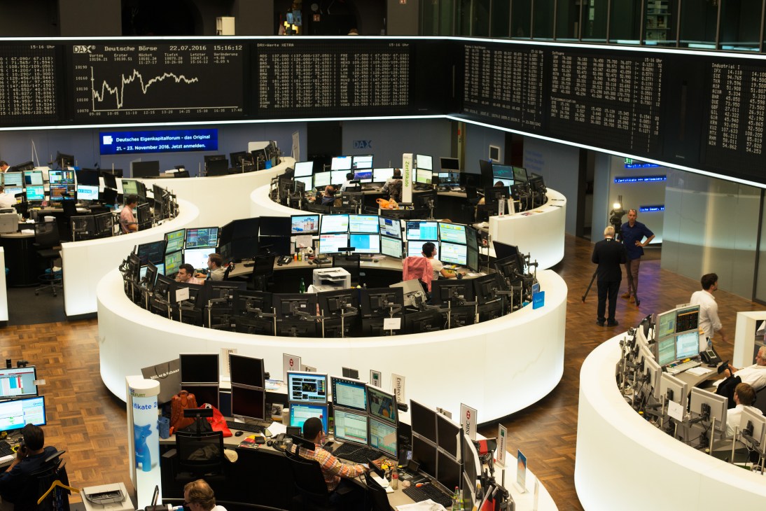 Deutsche Börse trading floor with curved white desks, multiple monitors displaying stock data, and traders at workstations.