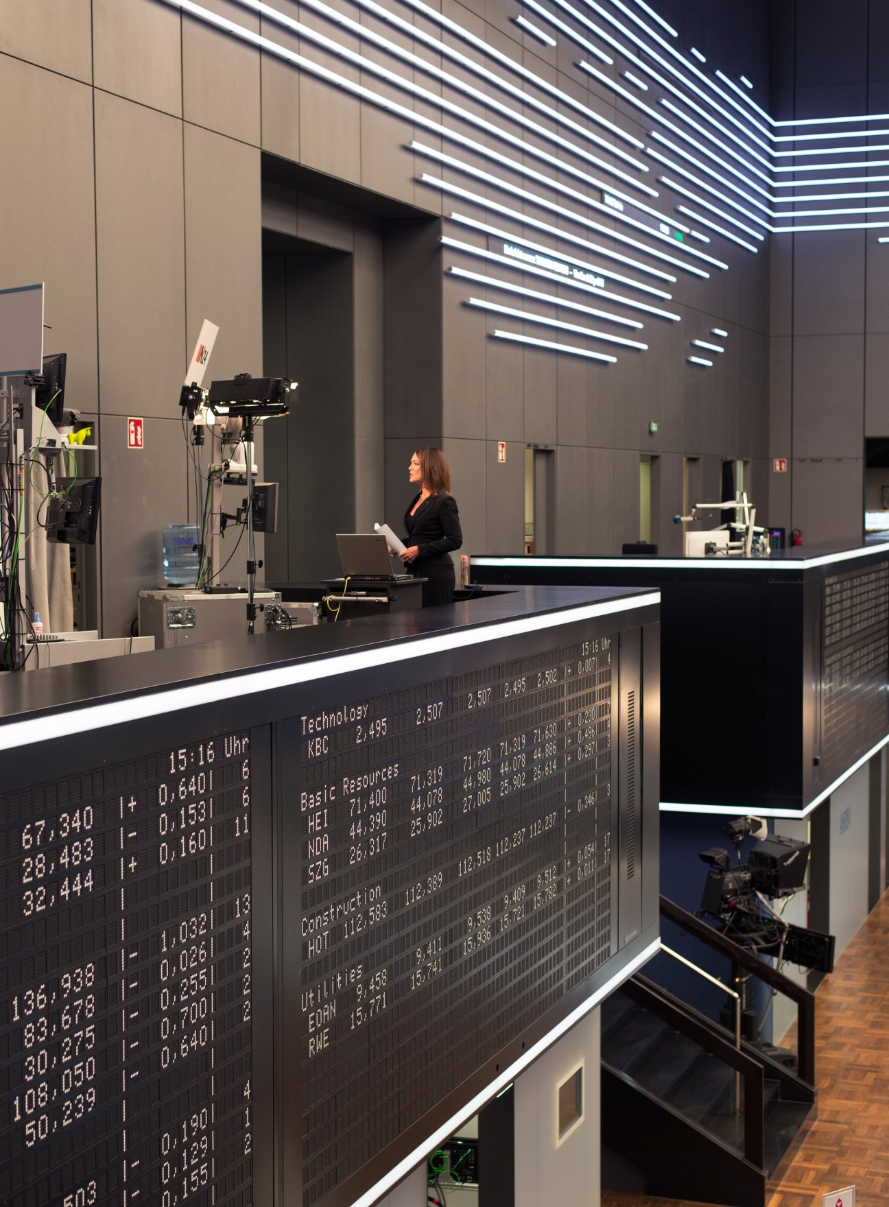 Woman reporting live from a trading desk with stock market data displayed on screens at Deutsche Börse.