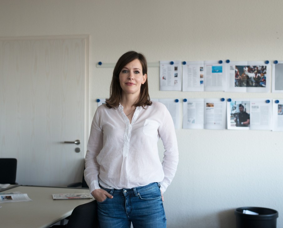 Melanie Mühl, editor of 'Die Woche', stands in an office with newspaper layouts pinned on the wall behind her.