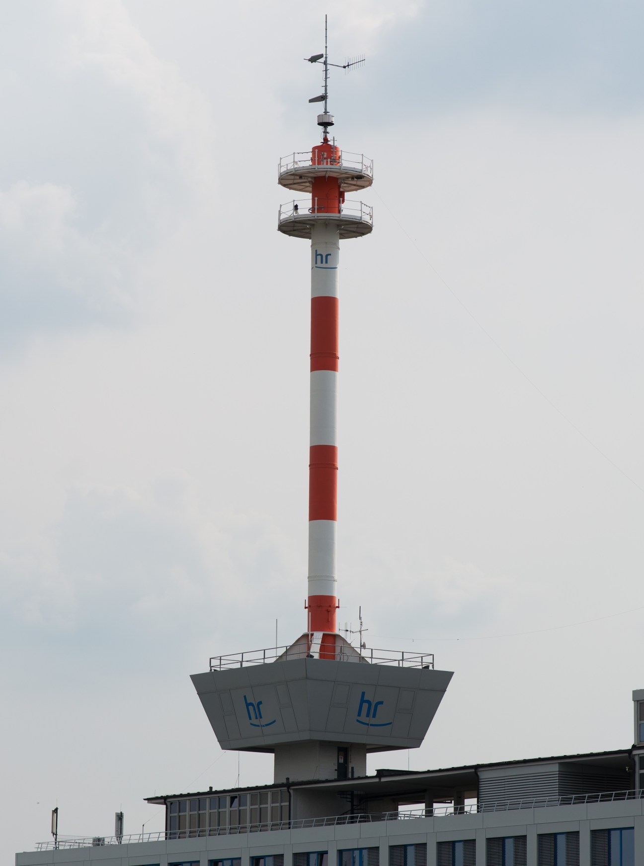 Red and white striped HR television transmission tower with antenna equipment and broadcast facilities.