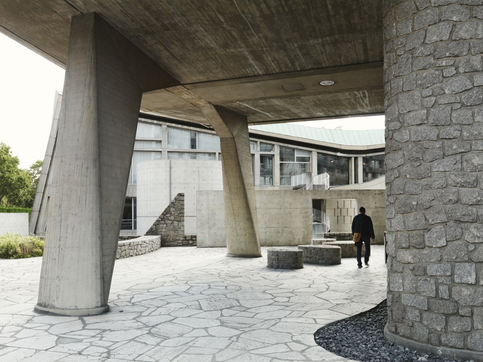 Modernist courtyard with concrete pillars, stone walls, and a person walking through Tadao Ando's meditation space.