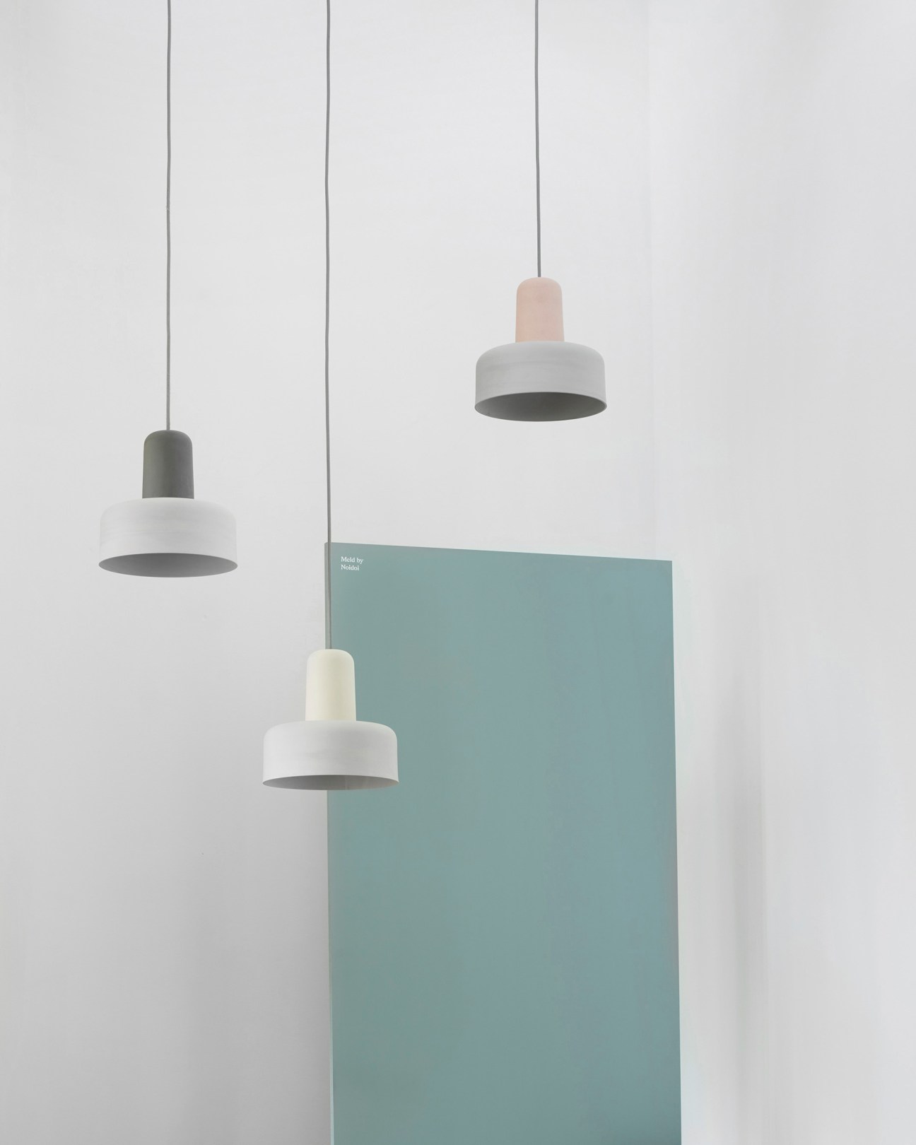 Three pendant lights with interlocking cylindrical cast stoneware shades in white and muted tones, hanging from thin cords against a white background.