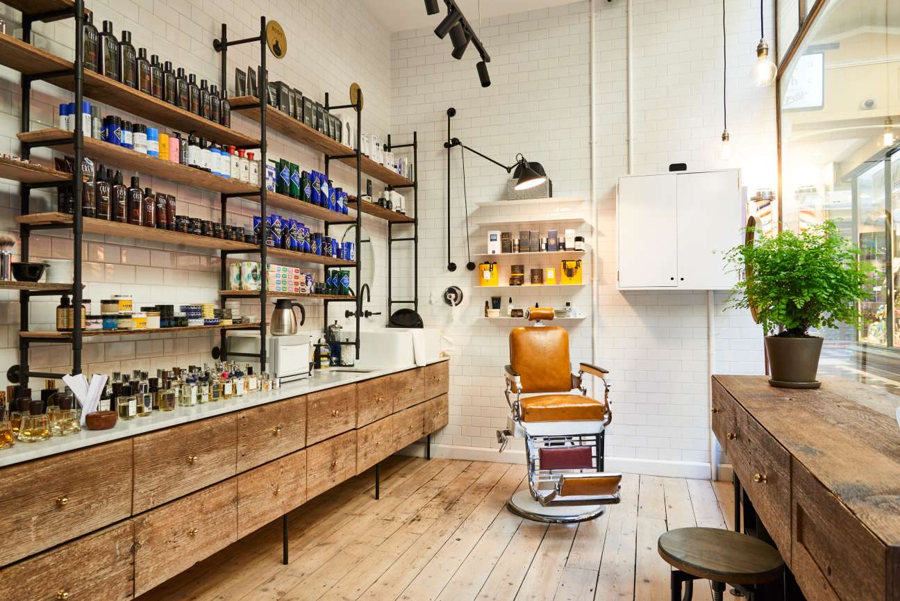 Men's Biz barbershop interior with wooden counter, leather barber chair, white subway tiles, and wooden shelves displaying grooming products.