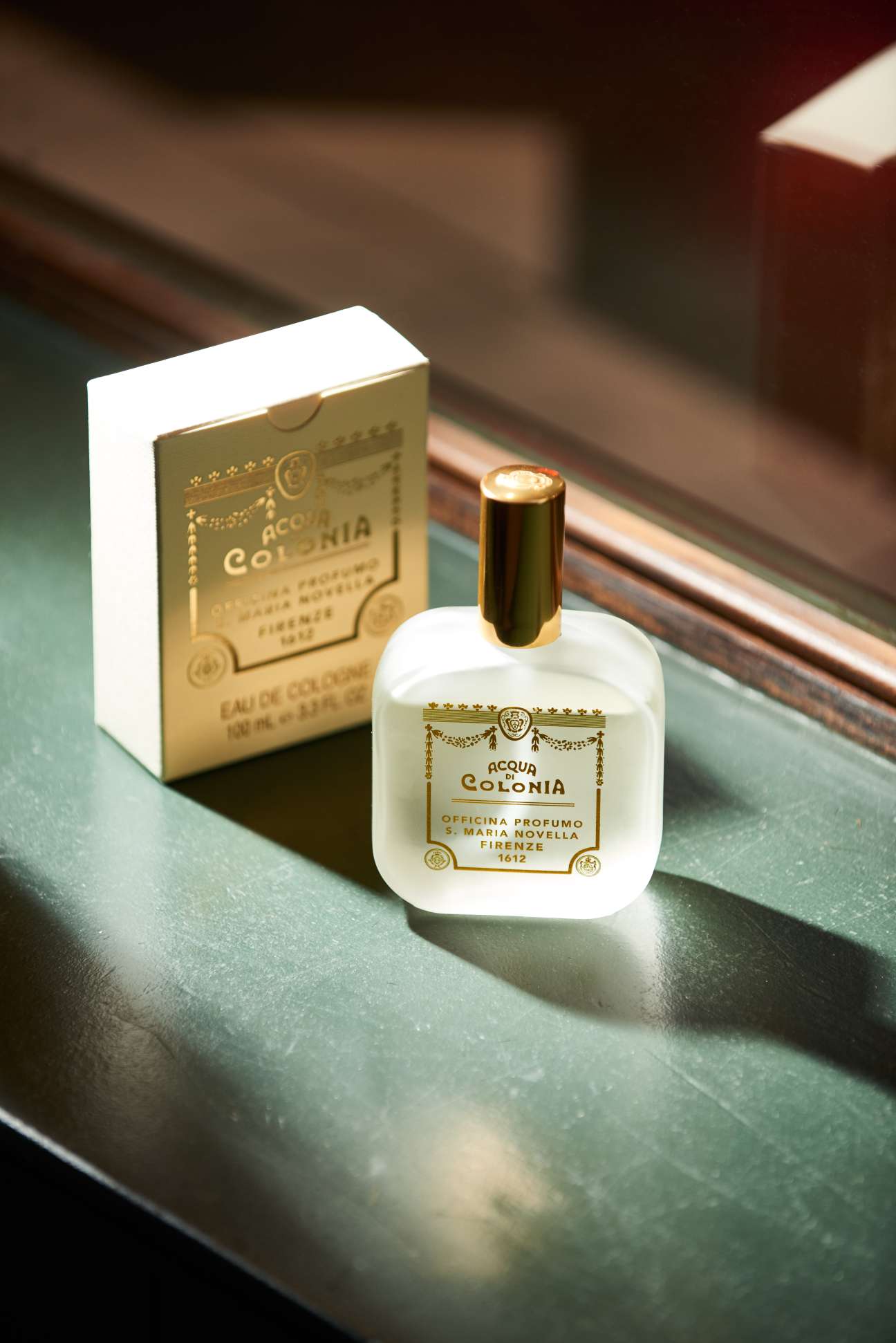 Acqua di Colonia fragrance bottle and box from Santa Maria Novella displayed on a green surface.