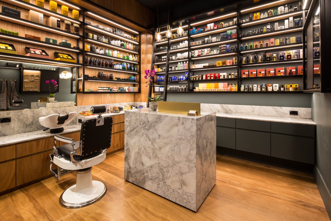 Men's Biz barber shop interior with marble counters, wooden shelving displaying grooming products, and a black barber chair.