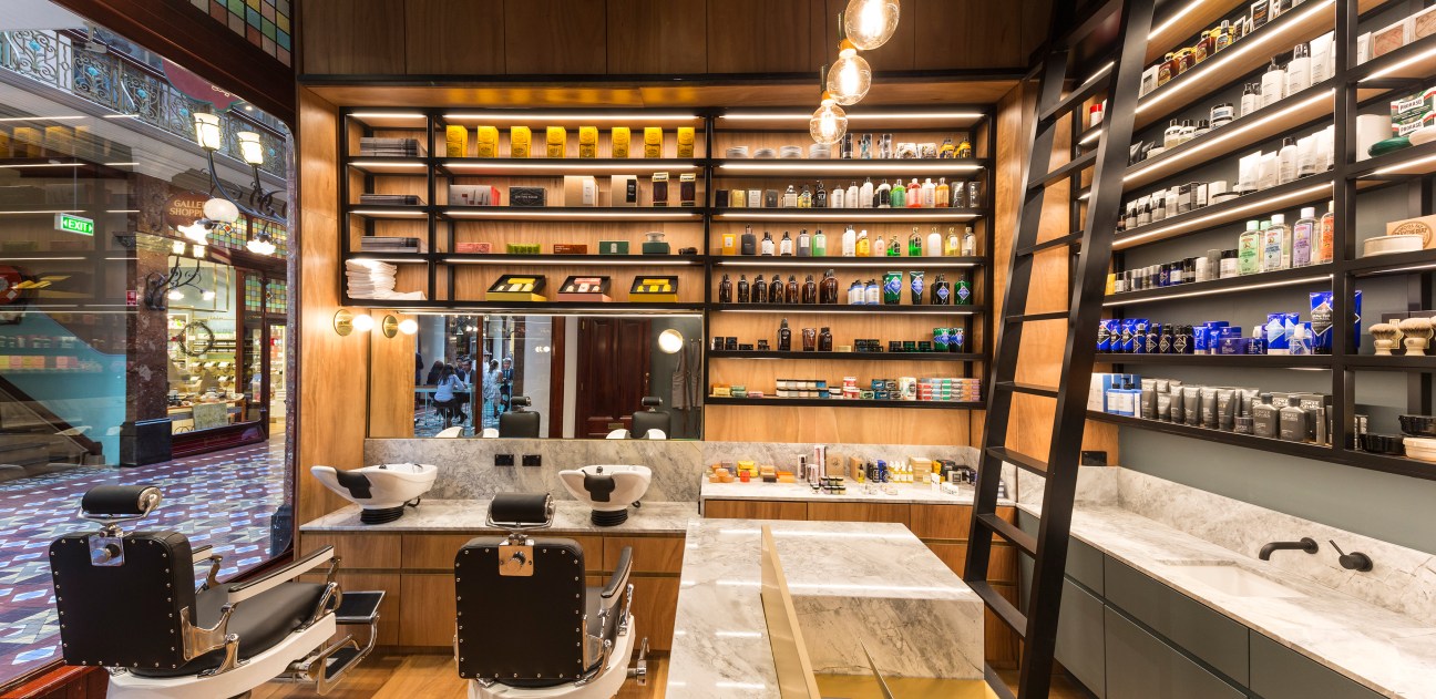Men's Biz grooming shop interior with wooden shelving, marble counters, barber chairs and product display.