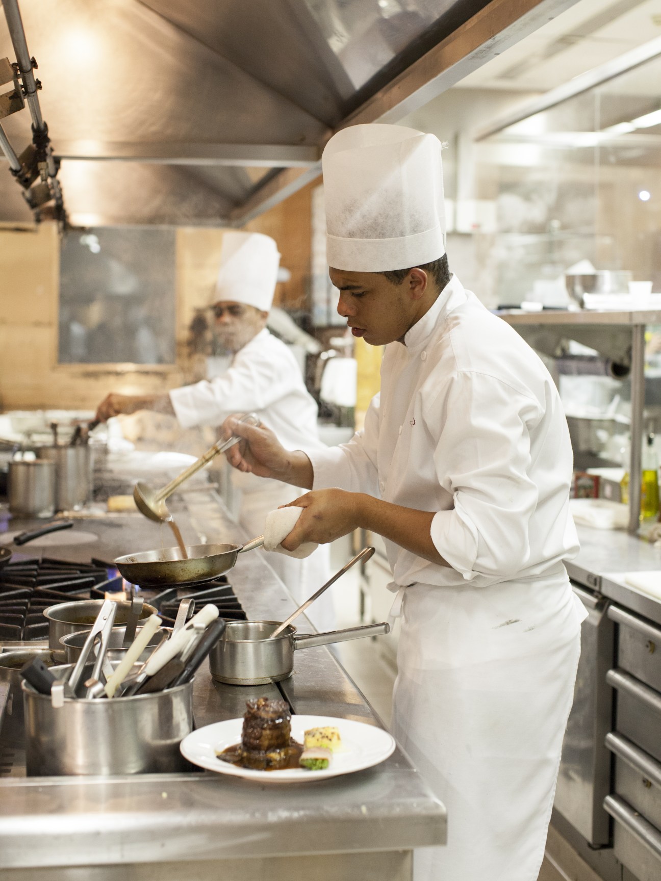 Chef in white uniform and chef's hat cooking in a professional kitchen at Fasano restaurant.