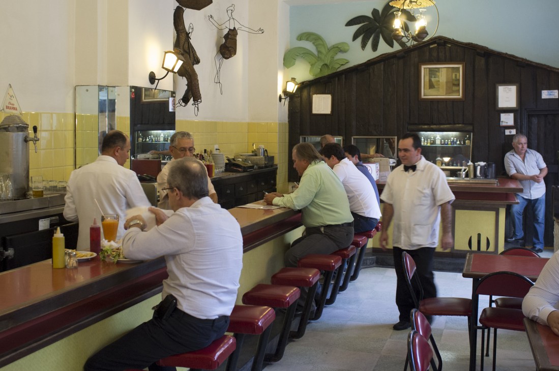 Interior of Frevinho restaurant with patrons seated at counter and vintage yellow tile walls with dark wood accents.