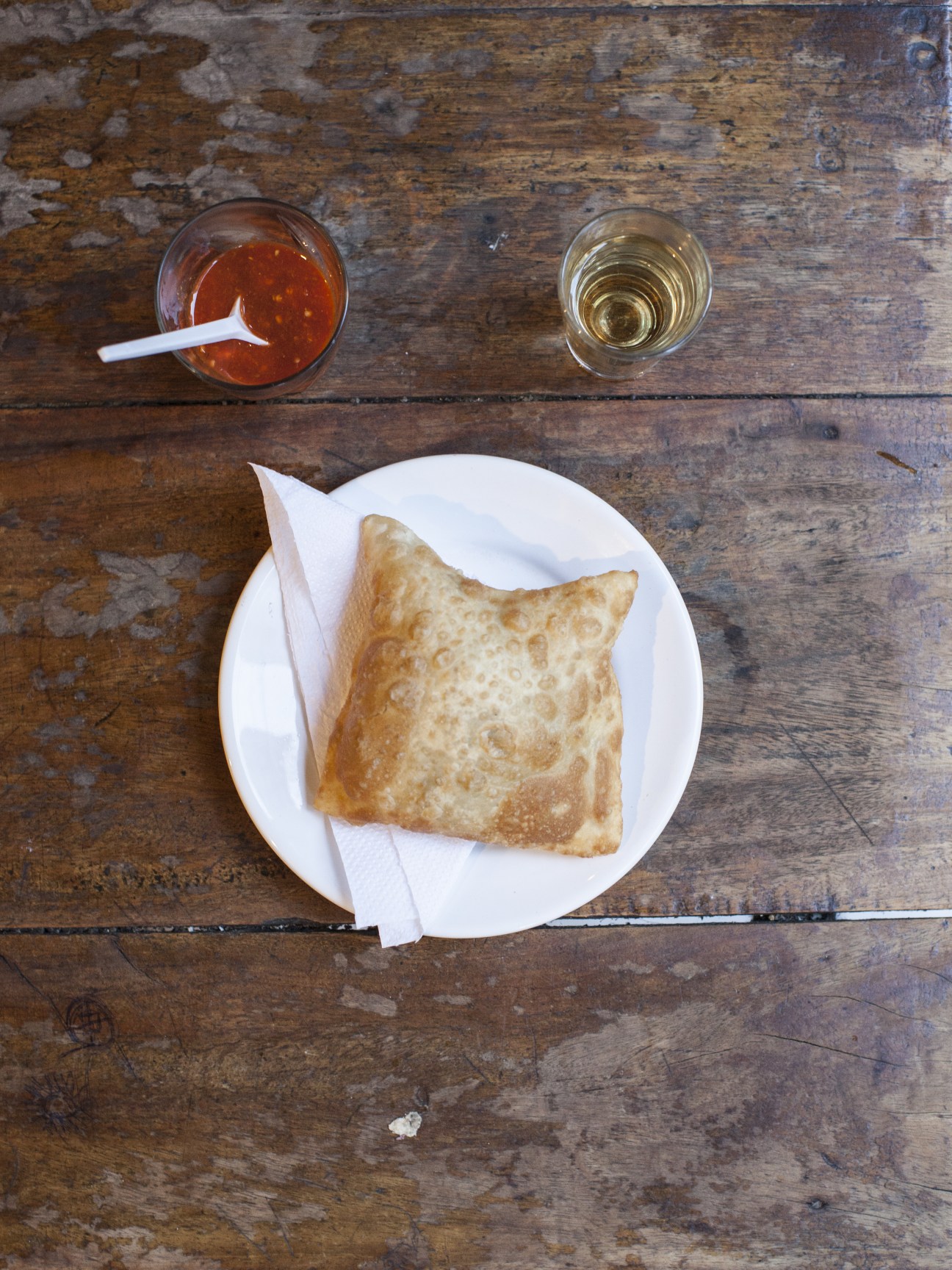 Fried pastel pastry on white plate with cachaça and white wine on rustic wooden table.