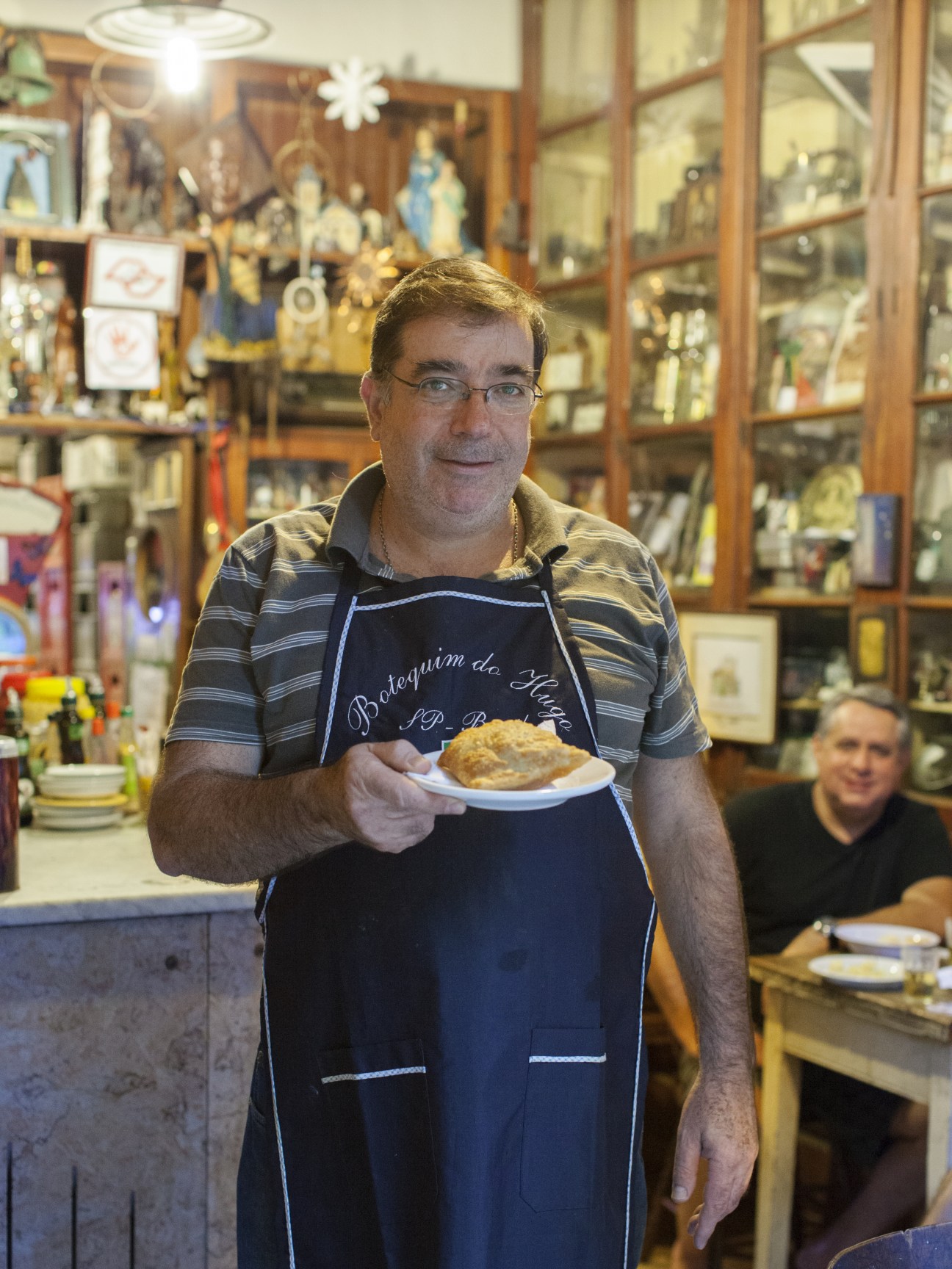 Hugo Cabral Filho holds a plate of food in his apron at Botequim do Hugo restaurant.