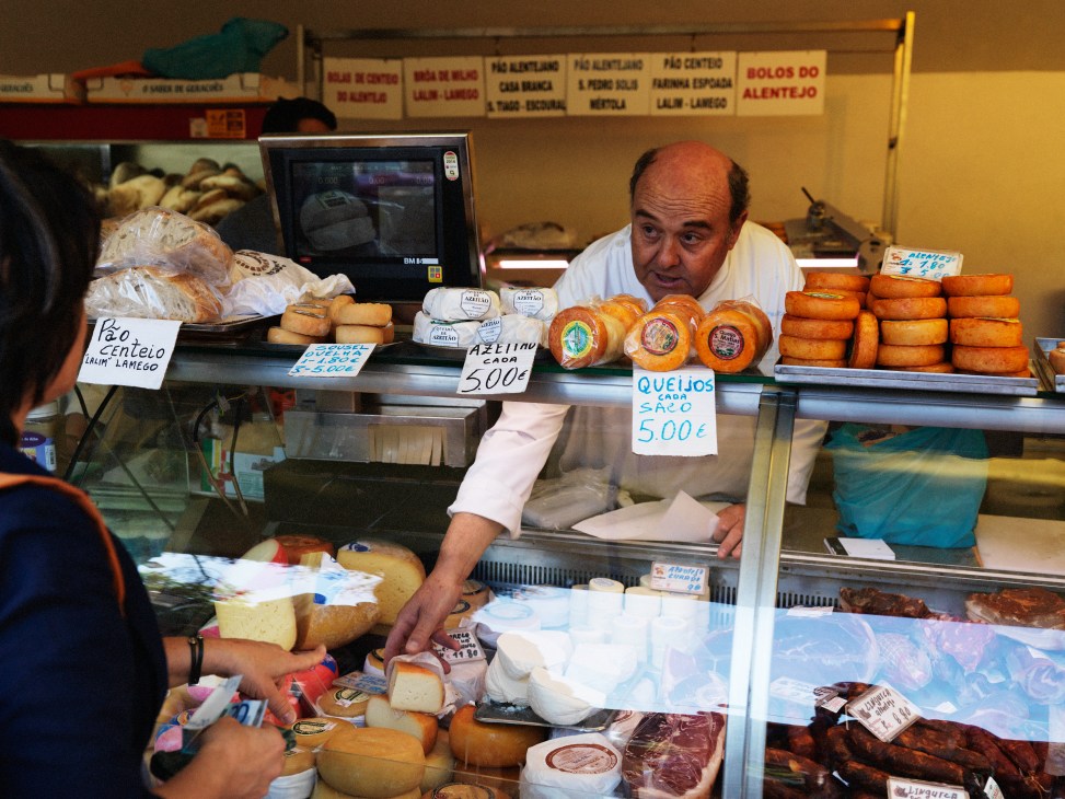 Cheese seller at Cascais town market displaying various Portuguese cheeses including Azeitão.