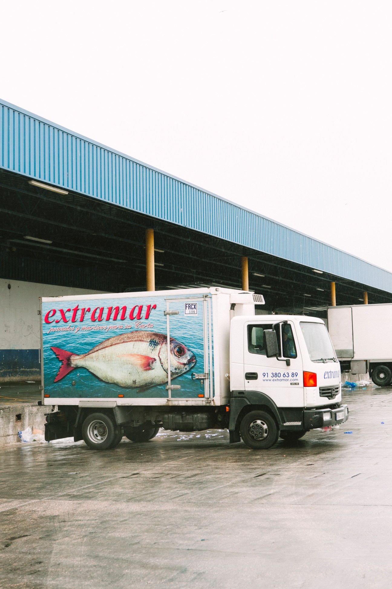 White refrigerated truck with Extramar branding and large fish image parked at Mercamadrid loading bay.