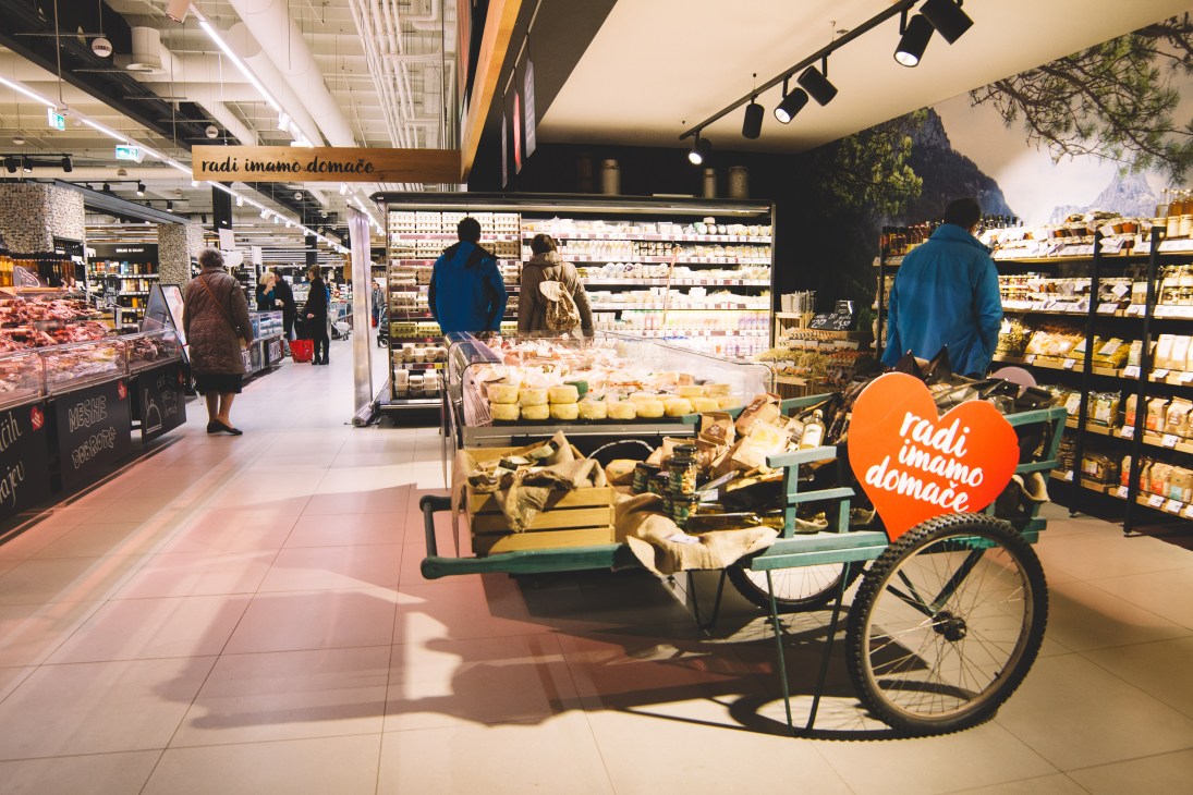 Mercator supermarket interior showing dairy products, local produce displays, and shoppers browsing the store.