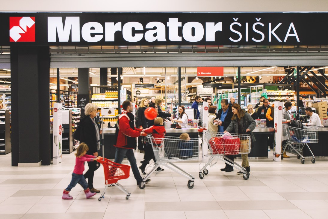 Mercator Siska supermarket storefront with customers shopping inside and red shopping carts outside.
