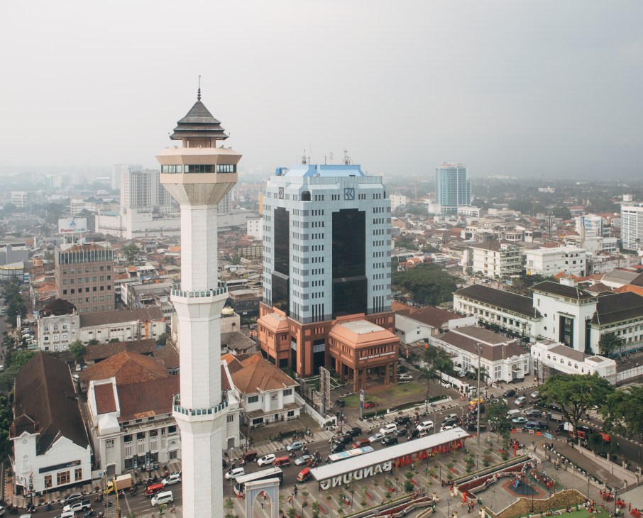 Aerial view of Bandung's Grand Mosque tower with cityscape and mountains in background.